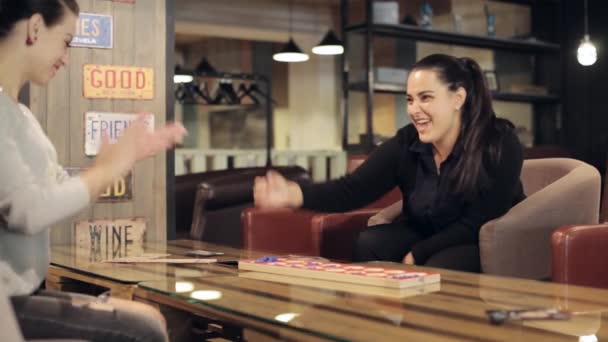 Two yong brunette womans play a board game in cafe. — Stock Video