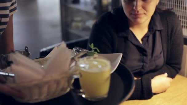 Молода жінка сидить у кафе і отримує торт з чаєм від офіціанта — стокове відео