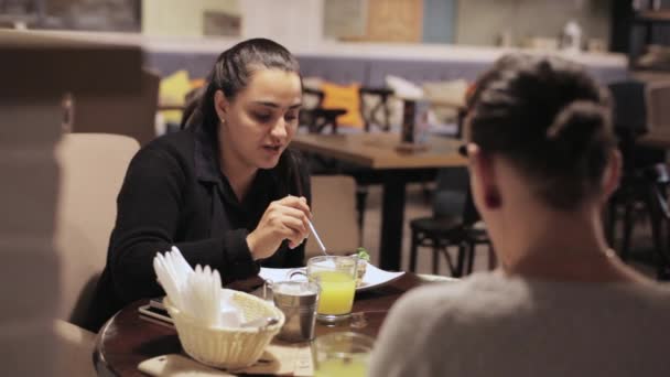 Dos mujeres jóvenes comiendo y hablando en un café — Vídeos de Stock