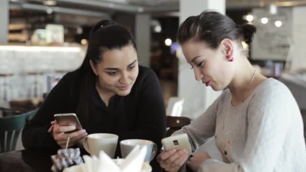 Twee jonge vrouwen zijn praten en het gebruik van smartphone iets grappig te tonen. — Stockvideo