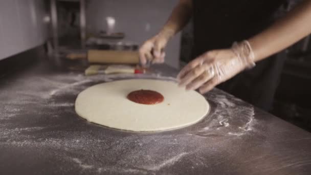 Chef-kok uitstrijkjes rode saus op het deeg voor pizza. — Stockvideo
