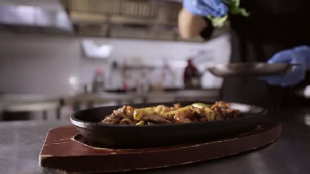 Chef ajoutant des herbes à la poêle avec des légumes et de la viande sur un stand en bois . — Video