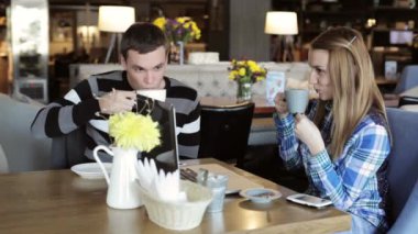 Erkek ve kız kafede. İnsanlar kullanmak laptop ve akıllı telefonlar, konuşma ve içecek kahve.