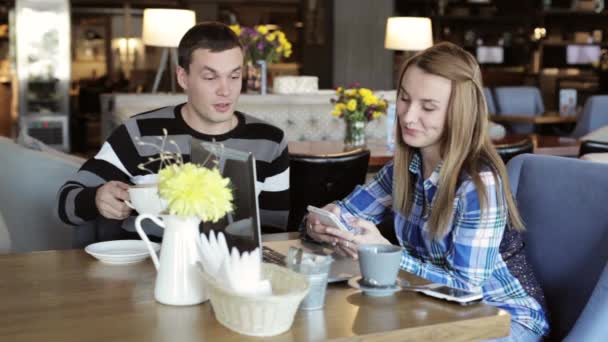 Jongen en meisje in café. Mensen gebruiken laptop en smartphones, praten en drinken koffie. — Stockvideo