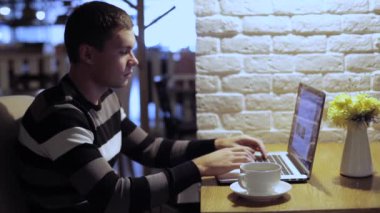 Kafede dizüstü ve içecek kahve üzerinde çalışan yakışıklı adam