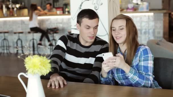 女人和男人坐在咖啡馆中说话，看着手机在手 — 图库视频影像