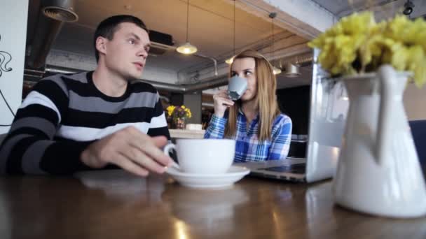 Двоє друзів сидять в кафе, розмовляють, п'ють каву і використовують ноутбук — стокове відео