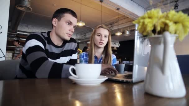 Dos amigos sentados en la cafetería, hablando, tomando café y usando el portátil — Vídeos de Stock