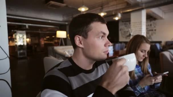 Jong koppel in café. Mannen drinken koffie terwijl het vrouwtje met smartphone — Stockvideo
