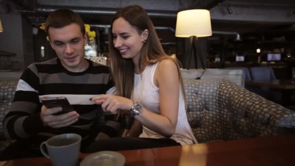 Attraktives junges Paar spricht und nutzt Smartphone im Café — Stockvideo