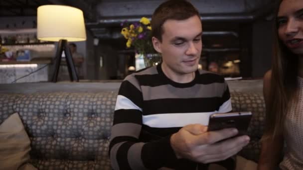 Привлекательная молодая пара разговаривает и пользуется смартфоном в кафе — стоковое видео
