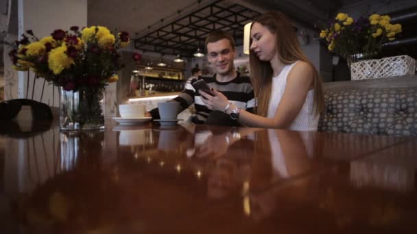 Двоє молодих кавказьких людей дивляться смартфон в кафе і сміються — стокове відео