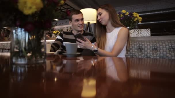 两个年轻的白种人看一部智能手机的一家咖啡馆和笑 — 图库视频影像