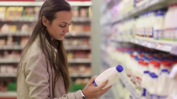 Jonge vrouw in een zuivel afdeling van de supermarkt een fles melk te kiezen. — Stockvideo