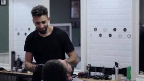 Barbier danse, chante et coupe barbe avec rasoir électrique dans un salon de coiffure . — Video