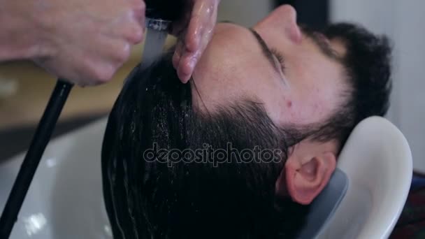 Мужчина парикмахер моет волосы клиенту в парикмахерской, крупным планом — стоковое видео