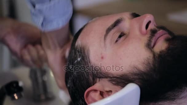 Мужчина парикмахер моет волосы клиенту в парикмахерской, крупным планом — стоковое видео