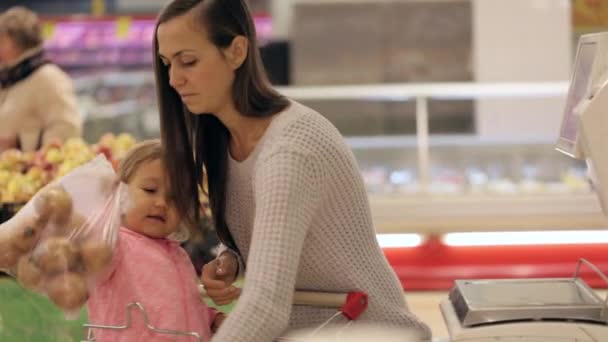 Молодая мама с маленькой дочерью весом овощи и фрукты в супермаркете — стоковое видео