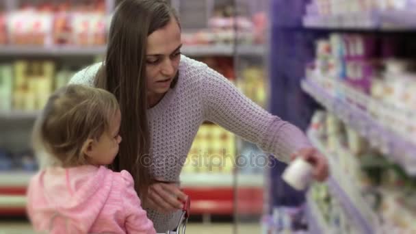 Vrouw met dochter plukken verse zuivelproducten in het koelvak — Stockvideo