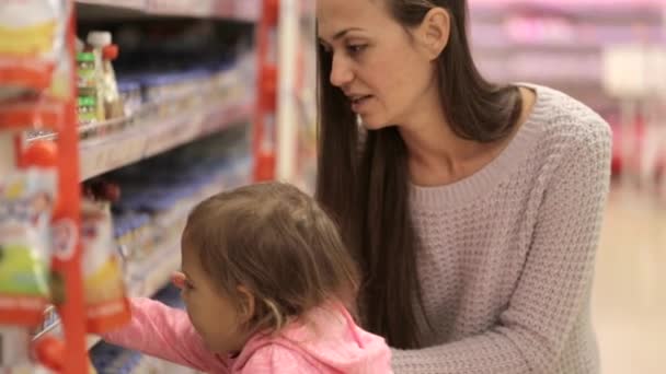 Молодая мать с маленькой дочерью делает покупки в супермаркете — стоковое видео