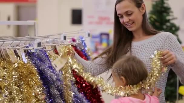 Junge attraktive Mutter mit kleinem Mädchen kauft Christbaumschmuck. — Stockvideo