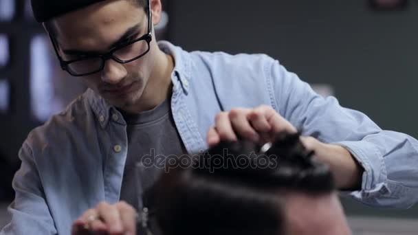 Young handsome barber making haircut of attractive bearded man in barbershop — Stock Video