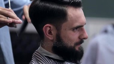 Genç yakışıklı berber berber dükkanında sakallı çekici bir adamın saçını kesiyor.