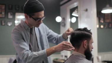 Genç yakışıklı berber berber dükkanında sakallı çekici bir adamın saçını kesiyor.