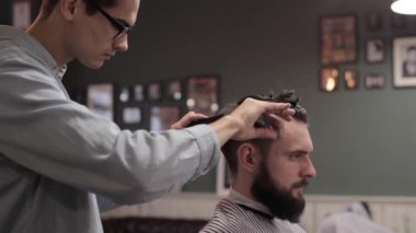 Genç yakışıklı berber berber dükkanında sakallı çekici bir adamın saçını kesiyor.
