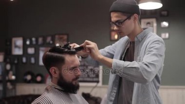 Genç yakışıklı berber berber dükkanında sakallı çekici bir adamın saçını kesiyor.