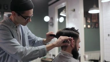 Genç yakışıklı berber berber dükkanında sakallı çekici bir adamın saçını kesiyor.