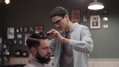 Genç yakışıklı berber berber dükkanında sakallı çekici bir adamın saçını kesiyor.