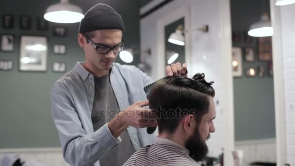 Pohledný muž s bradkou v holičství. Holič pracující s elektrický holicí strojek. — Stock video