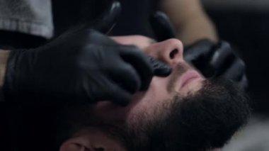 Bir berber bir losyon yüzünde genç erkek istemci ekleme Close-Up.