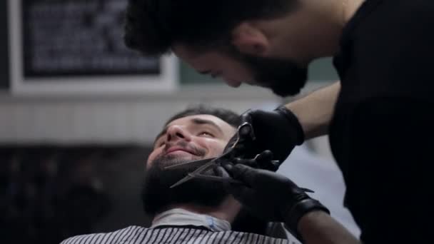 Proceso de peinado. Primer plano de un peluquero cortando la barba de un joven cliente masculino . — Vídeo de stock