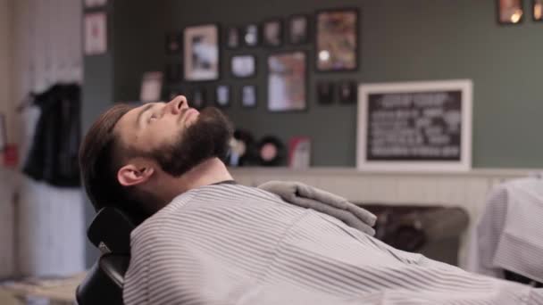 Barbeiro colocando uma toalha no peito do cliente e começa uma barba perigosa . — Vídeo de Stock
