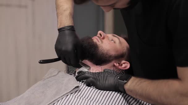 Barber shaves the beard of the client in the barbershop — Stock Video