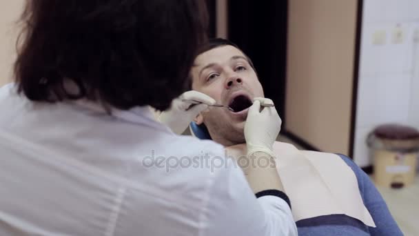 Dentista comprueba dientes de paciente masculino por espejo dental — Vídeo de stock