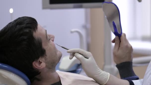 Femeie dentist care arată un dinte cu probleme la ea uitându-se la un pacient oglindă . — Videoclip de stoc