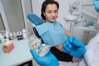 Diş hekimi hastayla. Diş hekimi diş bir model gösterilen.