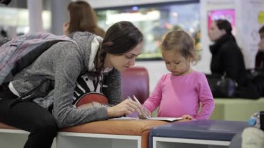 Anne ve kızı alıştırma kitabı ile havaalanında bekleme salonunda oturuyor