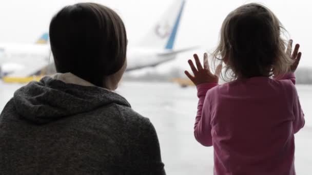 Mother and little daughter looking out the window at airport terminal — Stock Video