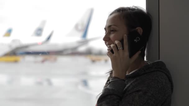 Mujer joven hablando por teléfono inteligente en el aeropuerto con avión en el fondo — Vídeos de Stock