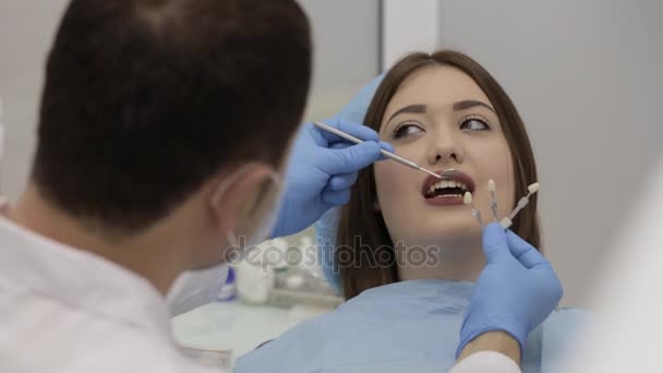 Dentista verificar e selecionar a cor dos dentes de jovem paciente do sexo feminino . — Vídeo de Stock