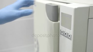 Diş hekimi eldivenli ellerle sterilizasyon için araçları koyar.