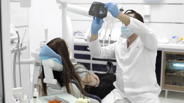 El dentista muestra a un paciente radiografías de los dientes en el consultorio dental — Vídeo de stock