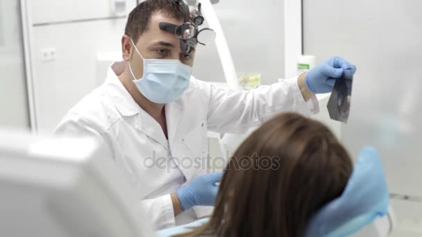 El dentista muestra a un paciente radiografías de los dientes en el consultorio dental — Vídeo de stock