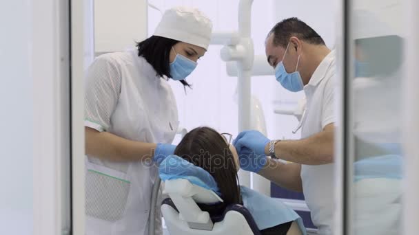 Dentista y enfermera haciendo procedimiento en paciente joven femenina en clínica moderna — Vídeo de stock