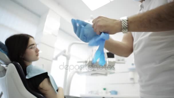 Homme dentiste mettre ses gants avec patient sur le fond — Video