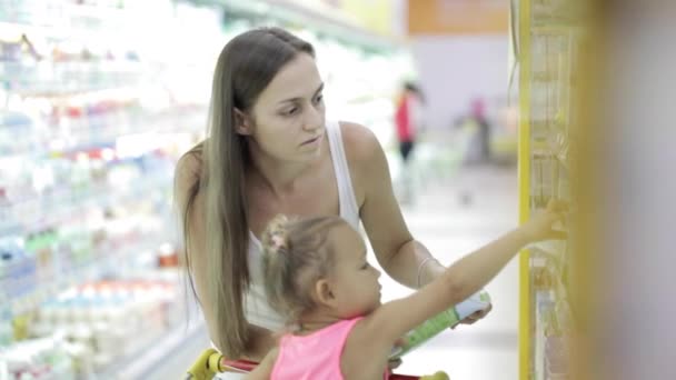 Молодая женщина с симпатичной дочерью выбирает молоко в супермаркете — стоковое видео